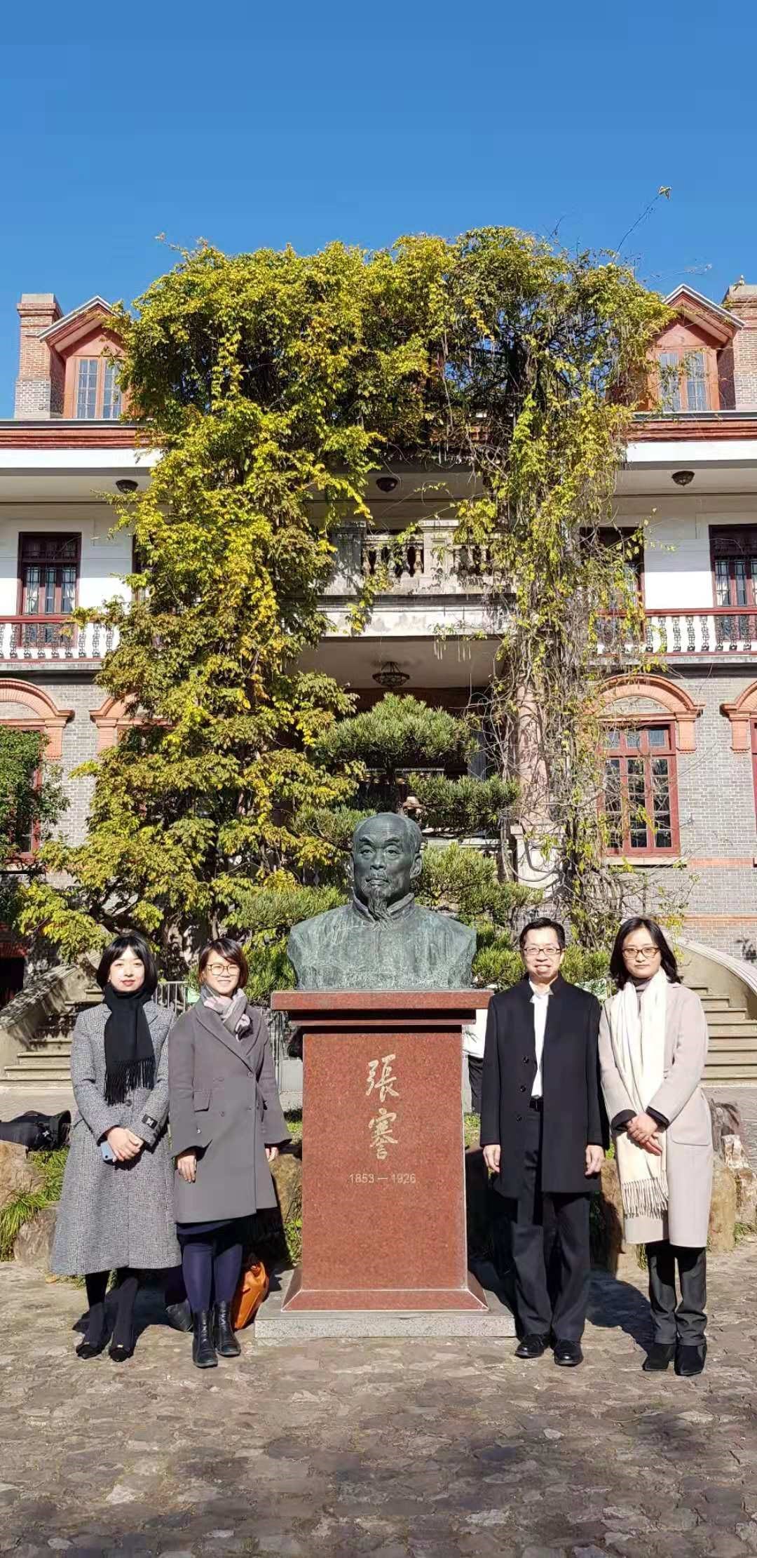 Four people stand by a statue of a man in front of a building with a tree.